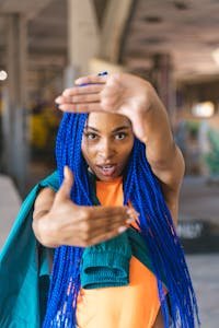 Vibrant portrait of a woman with blue braids, expressing creativity in urban setting.
